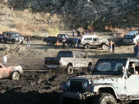 1978 Ford Bronco - Multiple off-road vehicles are bogged down in a muddy terrain, with onlookers observing the scene.