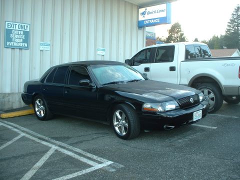 2000 Ford Crown Victoria - Black sedan and white pickup truck parked outside a building with 'Quick Lane Entrance' sign.