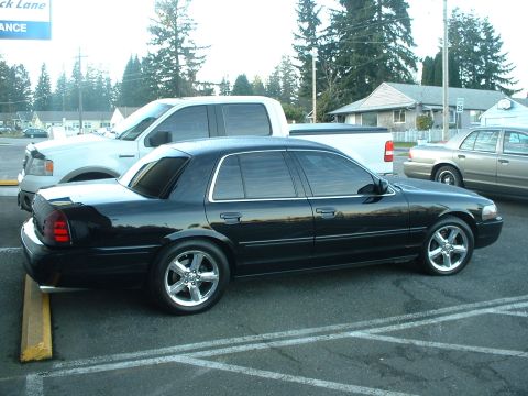 2000 Ford Crown Victoria - A black sedan is parked in a lot next to a white pickup truck and another sedan.