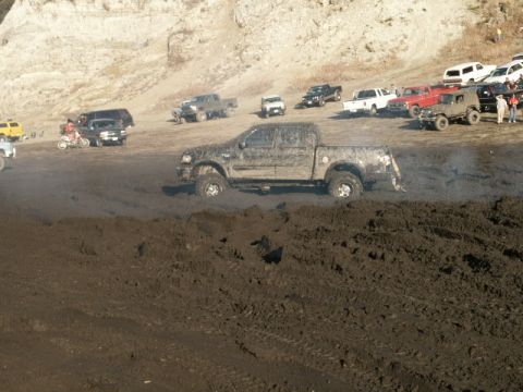 1978 Ford Bronco - Several vehicles are seen off-roading in a muddy area, with one pickup truck prominently stuck in the mire.