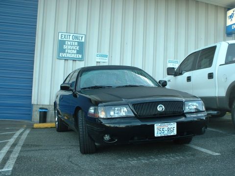 2000 Ford Crown Victoria - A black sedan with a Mercury emblem on the grille is parked next to a white pickup truck.