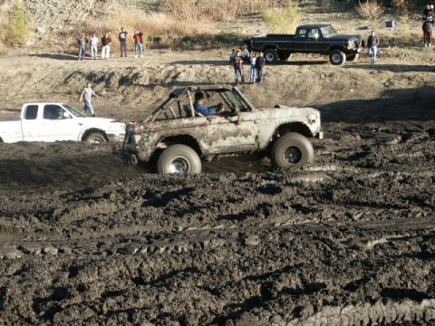 1978 Ford Bronco - A heavily mud-covered 1978 Ford Bronco navigates a muddy terrain, with other vehicles and spectators in the background.