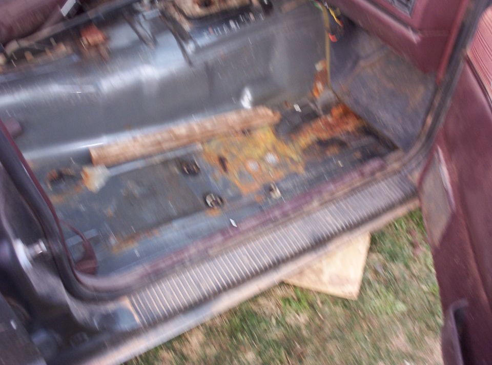 Rusty floor pan of a vehicle with door open showing corroded transmission tunnel