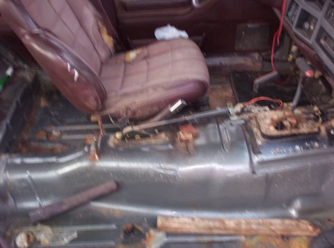 1987 Jeep Cherokee - The interior of a vehicle shows significant wear and tear, with rusted floor pans and damaged seats.
