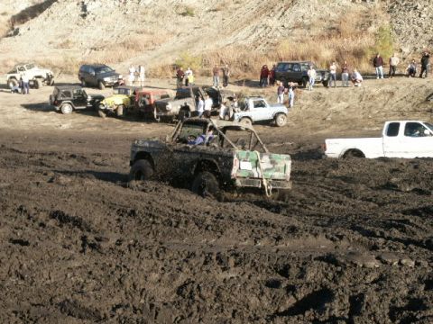 1978 Ford Bronco - Several off-road vehicles are stuck in a muddy terrain, with spectators gathered in the background.