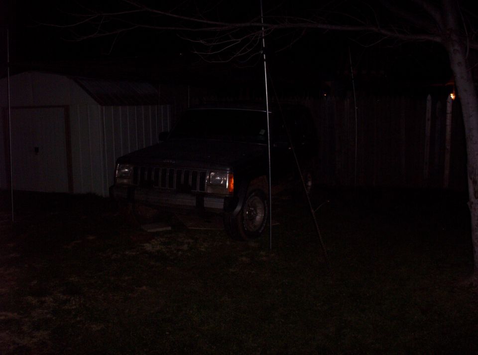 Front view of a dark colored Jeep Cherokee parked in a yard at night next to a shed