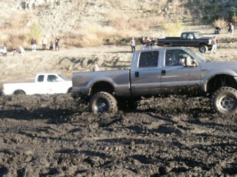 1978 Ford Bronco - A silver pickup truck navigates through a muddy terrain, with another white truck visible in the background.