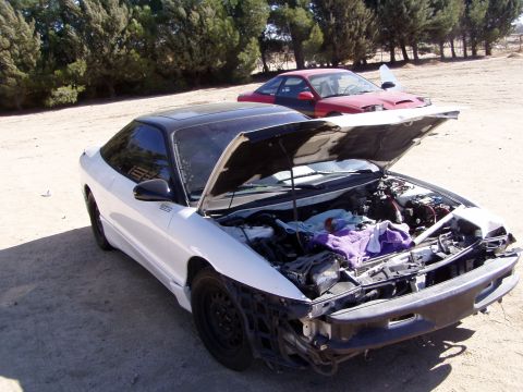 1993 Ford Probe - A white 1993 Ford Probe with its hood open sits in a dirt lot next to a red car.