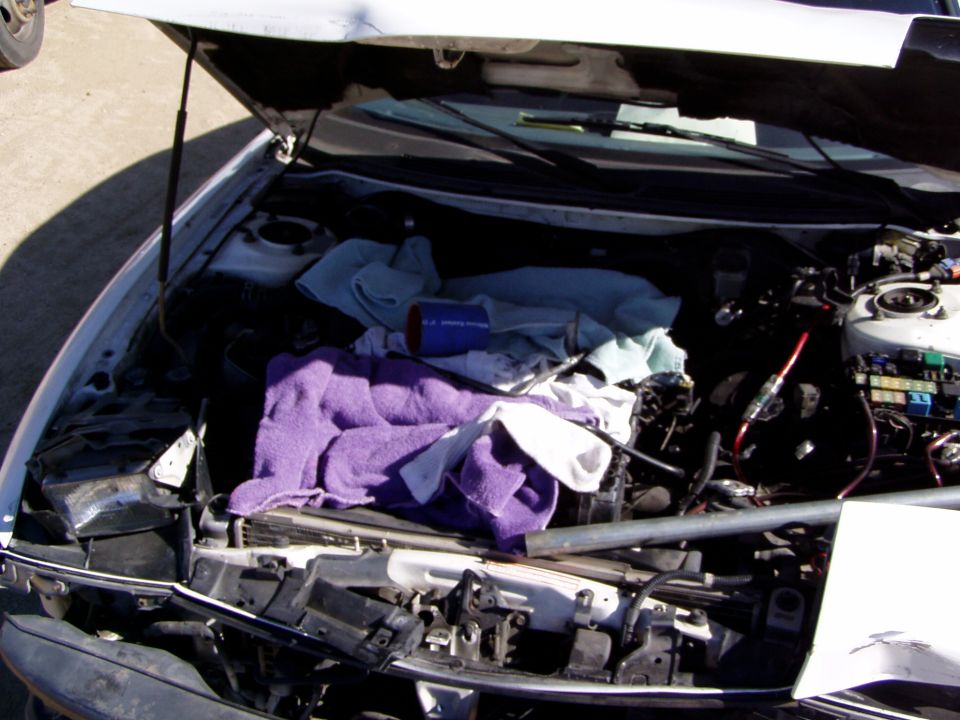 Car engine bay with hood open, covered in towels and parts. Supermotors.net logo visible