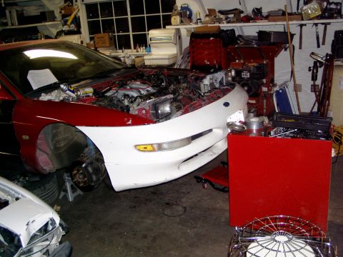 1993 Ford Probe - A 1993 Ford Probe is undergoing an engine swap in a cluttered garage, with another vehicle visible in the foreground.
