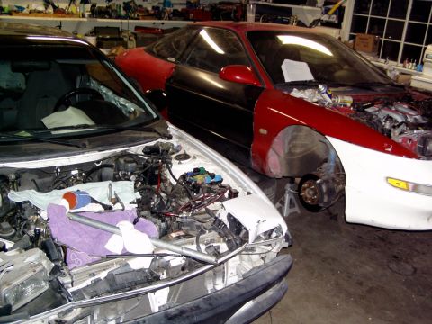 1993 Ford Probe - Two cars in a garage, one a red and black 1993 Ford Probe with its engine exposed and front end removed, the other a white car with its eng…