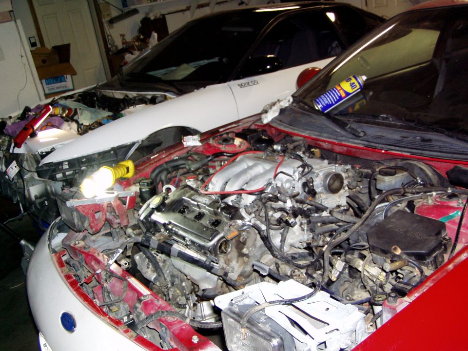 Two Ford Probe cars in a garage, engines disassembled. One is red, the other white