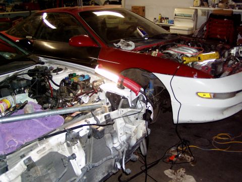 1993 Ford Probe - Two vehicles are undergoing mechanical work in a garage setting, with engines and front ends disassembled.