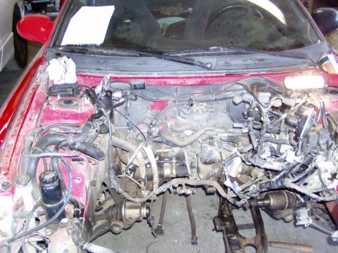 1993 Ford Probe - The engine bay of a red car is shown with the engine removed, revealing complex wiring and plumbing.