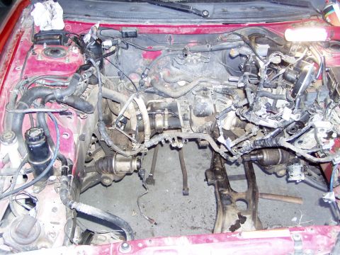 1993 Ford Probe - The engine bay of a red car is shown with the engine removed, revealing the drivetrain and suspension components.