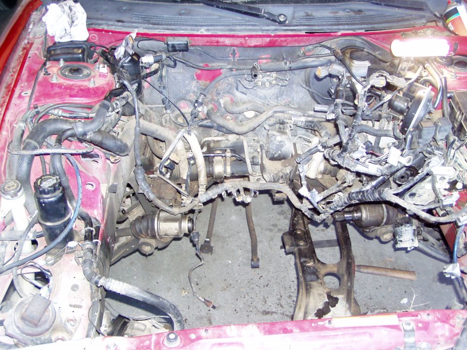 Red car engine bay with engine removed, showing drivetrain components