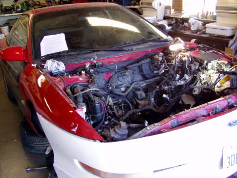 1993 Ford Probe - The engine bay of a red coupe is shown with the engine removed, revealing a cluttered workspace.