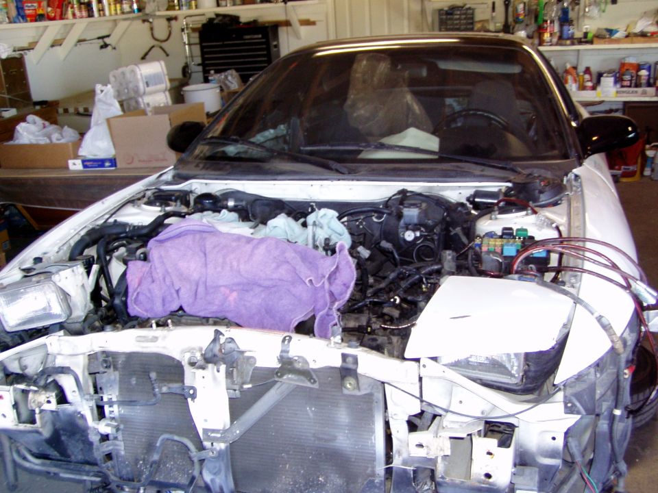 White 1993 Ford Probe with front end disassembled, engine bay open and covered with a purple towel