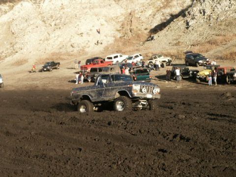 1978 Ford Bronco - Several off-road vehicles are gathered in a muddy area, with one truck prominently stuck in the foreground.
