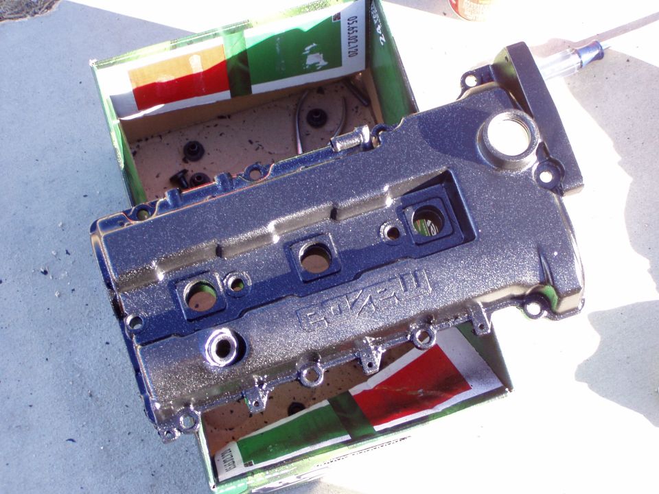 Silver engine valve cover with 'MAZDA' visible, resting in a box