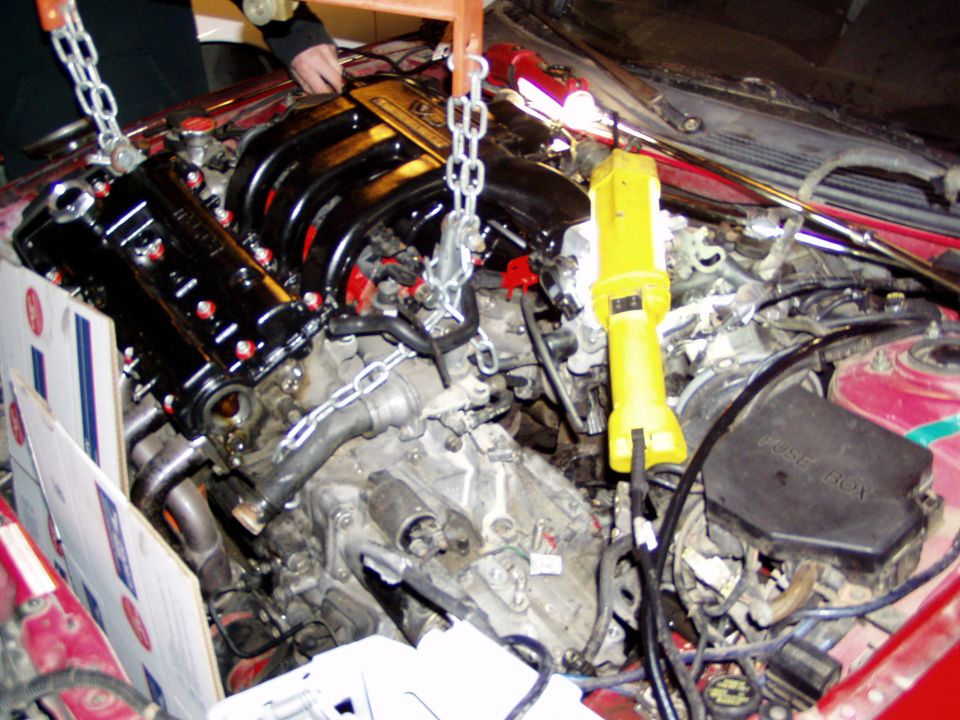 Engine bay with a black engine being lowered by chains, yellow work light attached