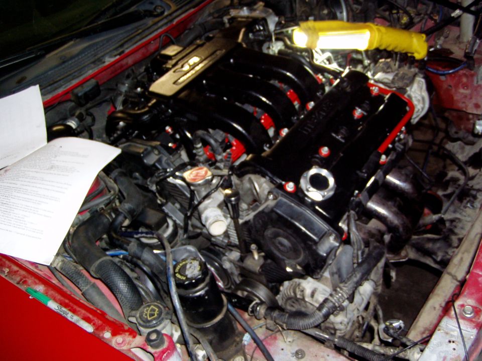 Engine bay with a V6 engine, possibly undergoing a swap. Manuals are open on the side