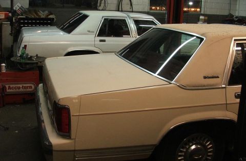 1991 Ford Crown Victoria LTD - Two sedans are parked in a garage, with the beige car in the foreground showing its rear side.