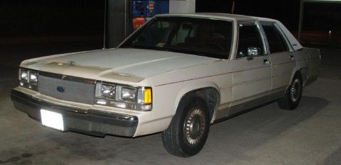 1991 Ford Crown Victoria LTD - This white 1980s Ford sedan is parked at a gas station, showing its 3/4 front profile.