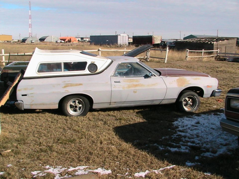 Side view of a 1973 Ford Ranchero with a camper shell and primer paint
