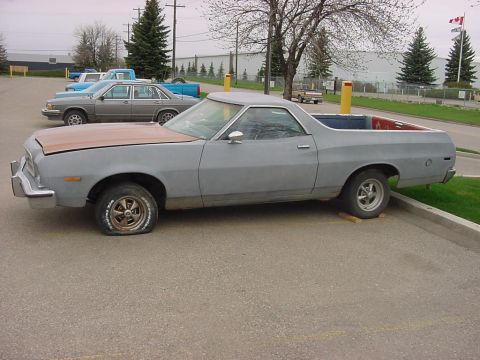 1973 Ford Ranchero - Side view of a 1973 Ford Ranchero in a parking lot, showing its utility bed and flat front tire.