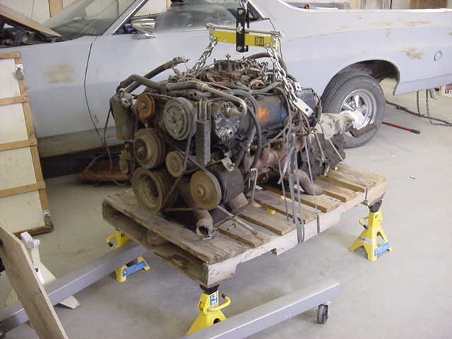 Engine removed from a car and sitting on a wooden pallet supported by jack stands