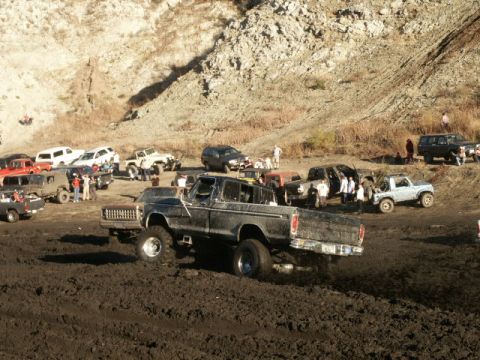 1978 Ford Bronco - Several off-road vehicles are gathered in a muddy area, with one truck prominently featured in the foreground.