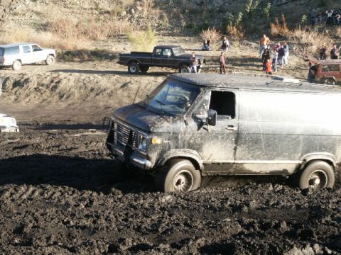 1978 Ford Bronco - A black van is stuck in deep mud, with other vehicles and spectators in the background.