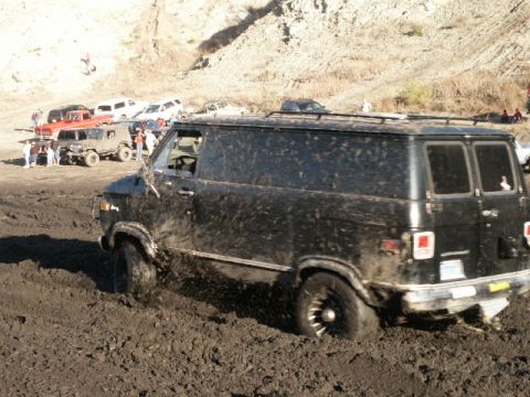 1978 Ford Bronco - A black van is stuck in mud, with other vehicles and people visible in the distance.