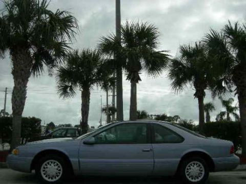 1991 Ford Bronco - A 1991 Ford Thunderbird is parked under a cloudy sky with palm trees in the background.