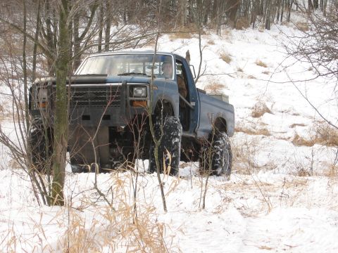 1979 Ford Bronco - A lifted blue pickup truck navigates a snowy, wooded area during winter.