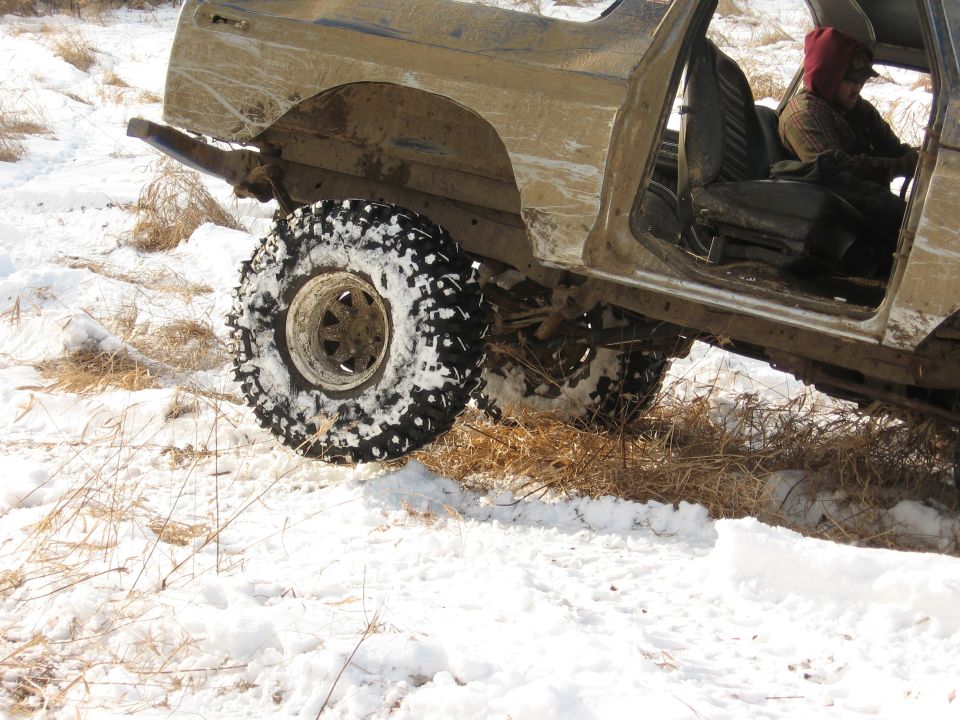 Mud-covered 1978 Ford Bronco with snow on tires, seen from the side with the driver's door open