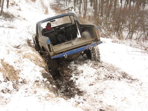 1979 Ford Bronco - A blue off-road vehicle struggles for traction in a muddy, snow-covered trail.