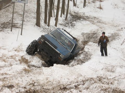 1979 Ford Bronco - A person observes a blue SUV that has slid off a snowy road and is stuck in a ditch.