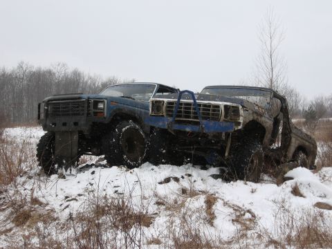 1979 Ford Bronco - Two heavily modified trucks, including a blue 1979 Ford Bronco, are stuck in a snowy landscape.