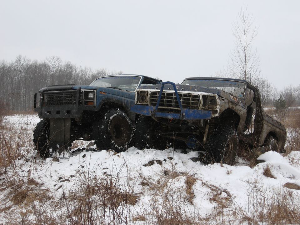 Blue 1979 Ford Bronco and a brown truck in snow