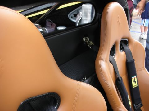 1998 Ford Crown Victoria - Two tan leather bucket seats with black racing harnesses and a Ferrari shield emblem inside a sports car cabin.