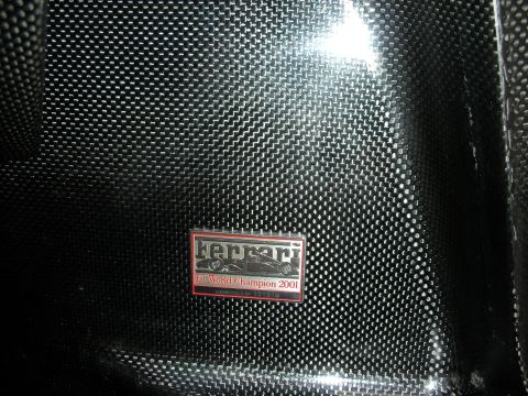 1998 Ford Crown Victoria - Close-up of a glossy carbon-fiber surface bearing a red Ferrari 'F1 World Champion 2001' enamel emblem.
