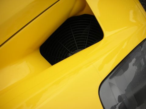 1998 Ford Crown Victoria - black mesh-covered air intake set into the yellow rear bodywork of a sports car, taillight visible below.