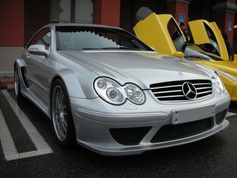 1998 Ford Crown Victoria - Silver Mercedes AMG coupe with widebody fenders parked front-on, a yellow car with raised door beside it.