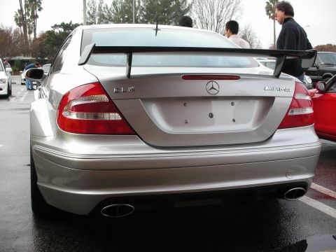 1998 Ford Crown Victoria - Rear view of a silver Mercedes-Benz CLK AMG coupe fitted with a tall rear wing, parked among other cars on a wet lot.