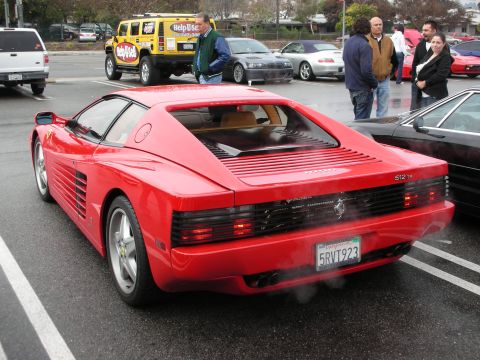 1998 Ford Crown Victoria - Rear three-quarter view of a red Ferrari 512 TR with side strakes, parked on a wet lot with people and a Hummer behind.