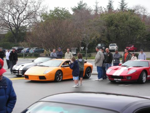 1998 Ford Crown Victoria - Crowd gathered around an orange Lamborghini, a red Ford GT, and a striped car at an outdoor car meet on a gray day.