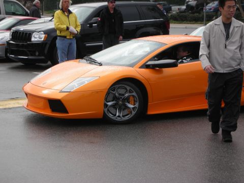 1998 Ford Crown Victoria - Orange Lamborghini Murcielago seen front three-quarter on a wet lot as a man in a gray jacket walks past.