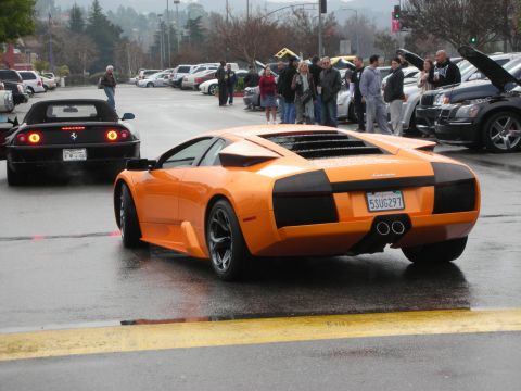 1998 Ford Crown Victoria - Rear view of an orange Lamborghini Murcielago next to a black Ferrari at a car gathering on a rainy day.
